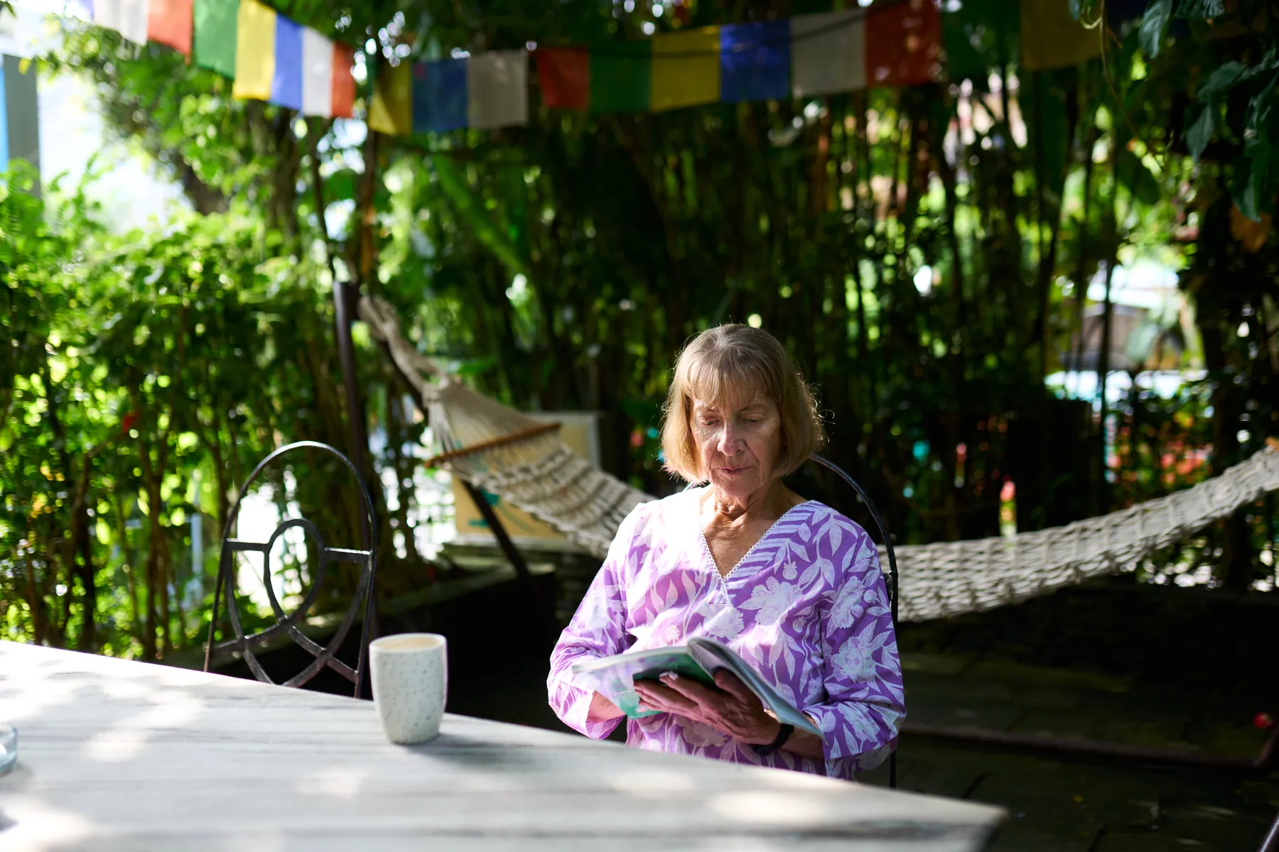 Guest reading with a cup of tea under prayer flags in the garden